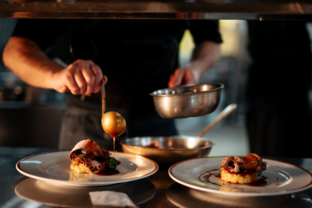 Koch garniert ein Gourmetgericht auf einem Teller und fügt kunstvoll eine Sauce hinzu.
