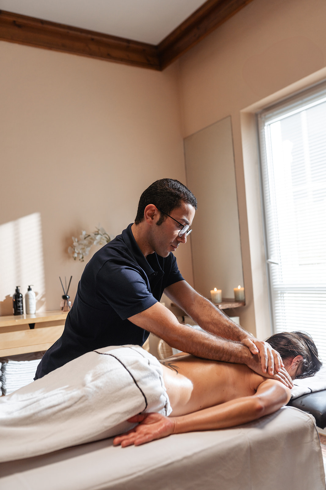 Masseur gibt eine entspannende Rückenmassage in einem Wellnessraum, umgeben von Kerzen und einer ruhigen Atmosphäre.
