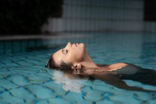 Frau entspannt sich im Wasser eines Schwimmbeckens und genießt die ruhige Atmosphäre.