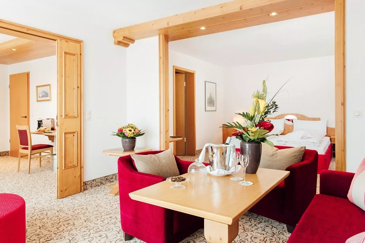 Hotelzimmer mit separatem Sitzbereich, einem Tisch mit Blumen, Champagner und Gläsern für einen luxuriösen Aufenthalt.