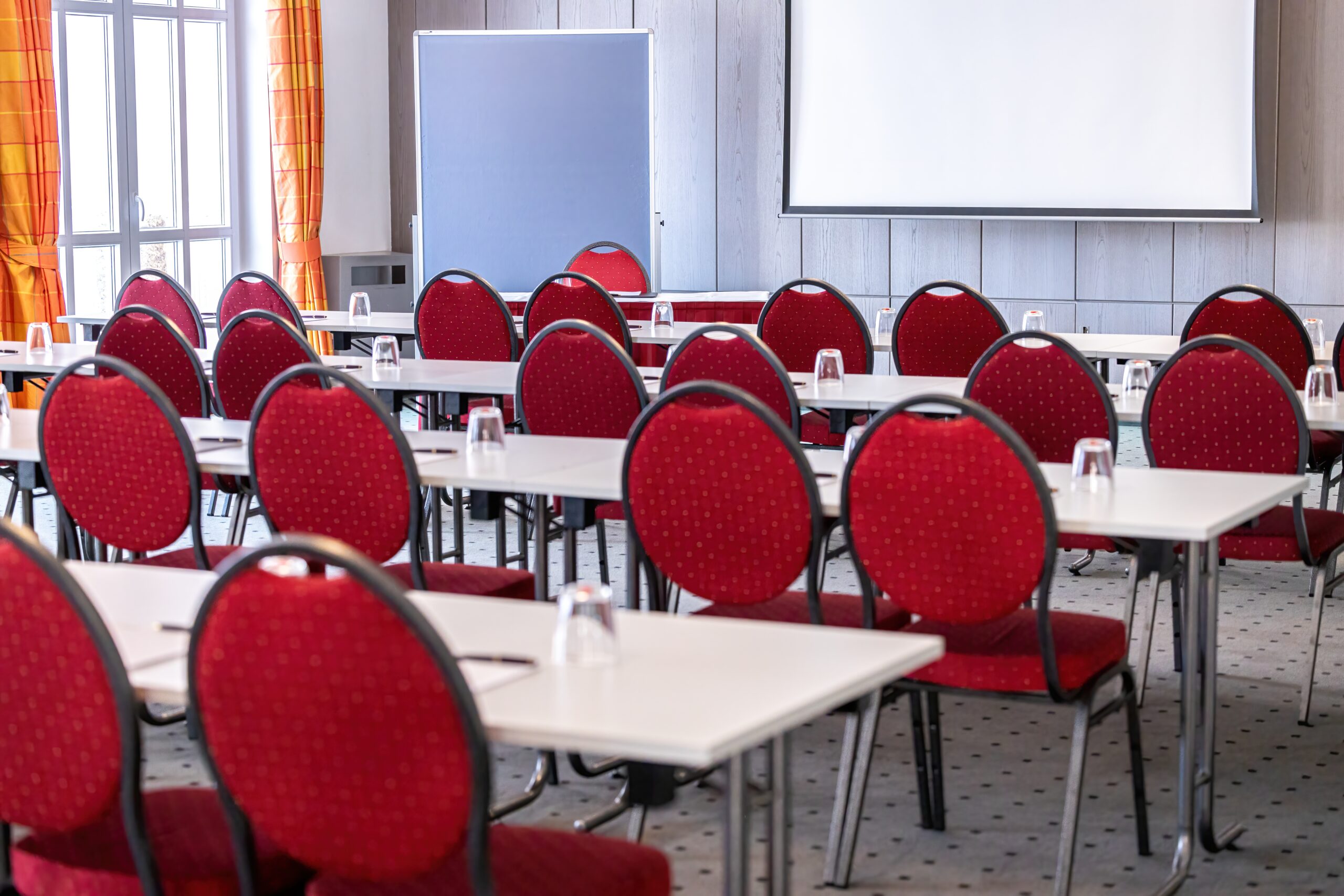 Konferenzraum mit roten Stühlen und Tischen, ideal für Seminare und Geschäftstreffen.