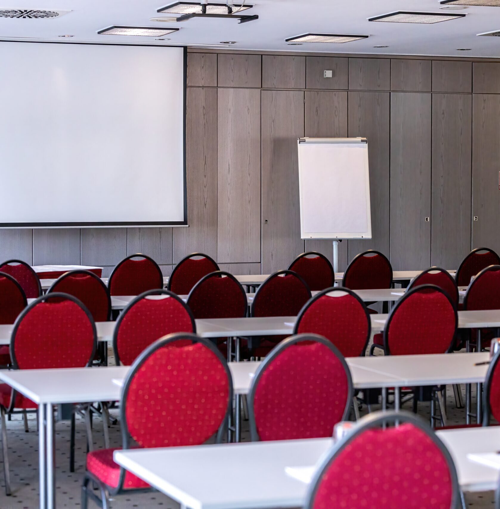 Seitlicher Blick auf einen Konferenzraum mit Tischen und roten Stühlen, ideal für Seminare und Schulungen