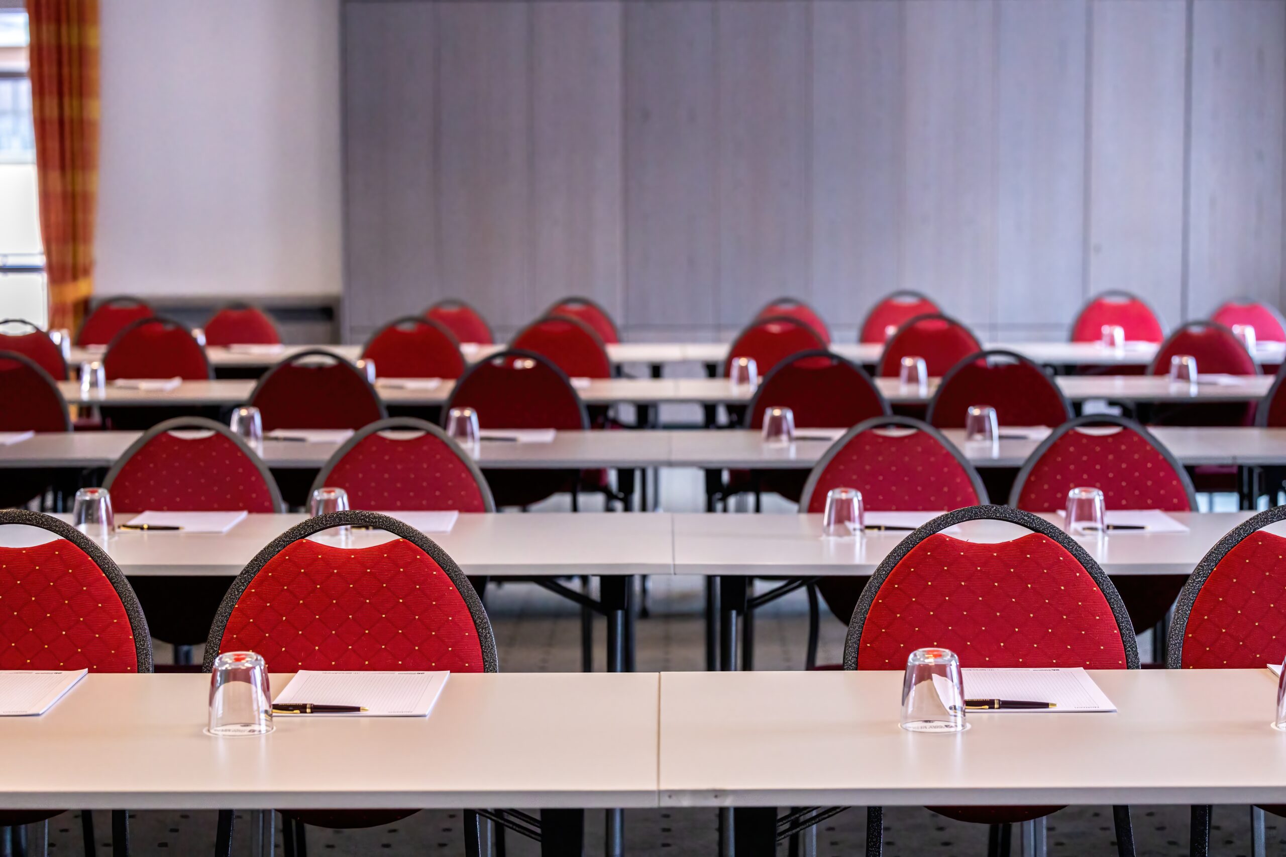 Besprechungsraum mit Tischen und roten Stühlen, ideal für Konferenzen und Veranstaltungen