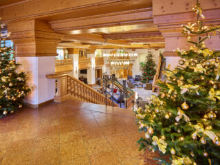 Festlich dekorierte Lobby mit geschmückten Tannenbäumen, Lichterketten und einem eleganten Treppenaufgang, ideal für festliche Anlässe oder Weihnachtsfeiern