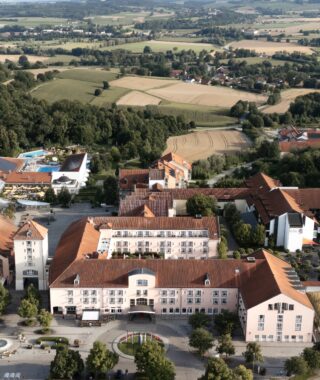 Luftaufnahme einer Hotelanlage mit gepflegten Gärten und angrenzenden grünen Feldern.